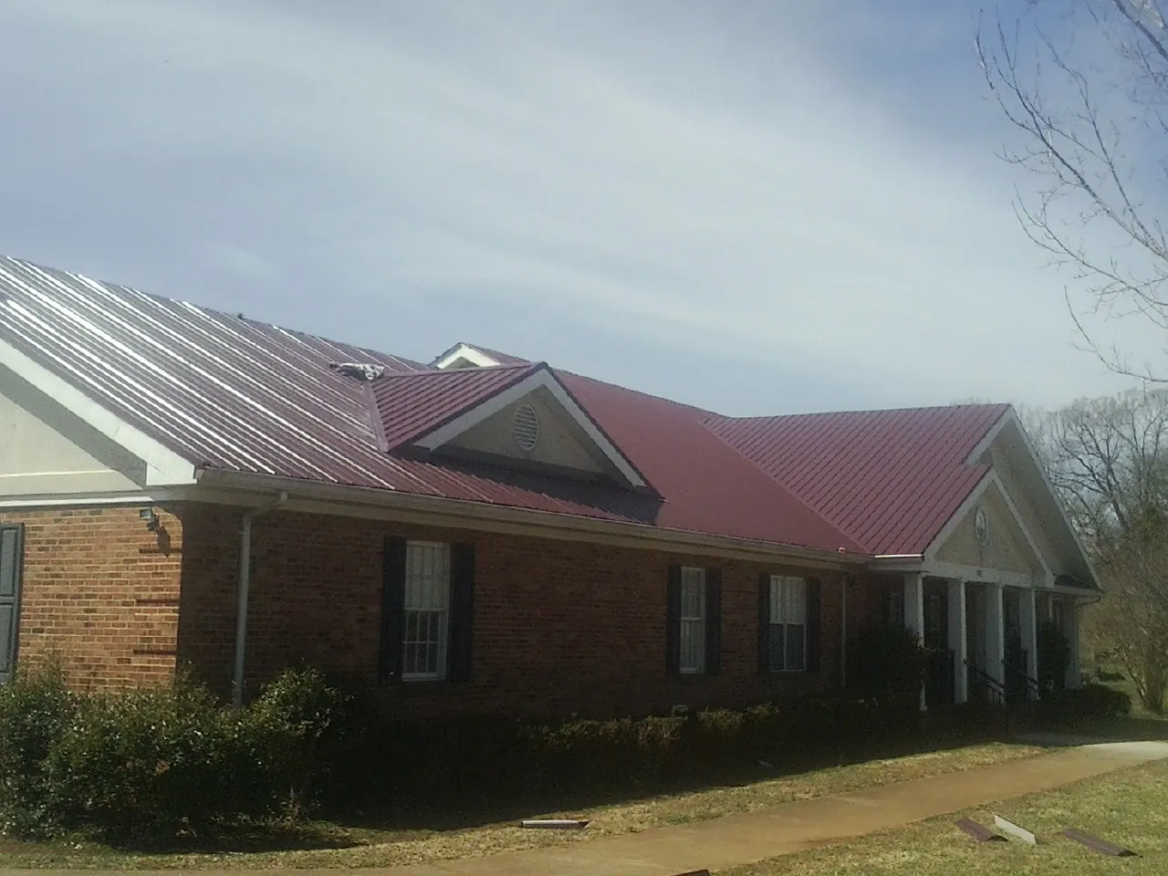 Red metal roof with gabled entries on a long brick building, from a Hail Damage Roof Repair job in Saint Albans