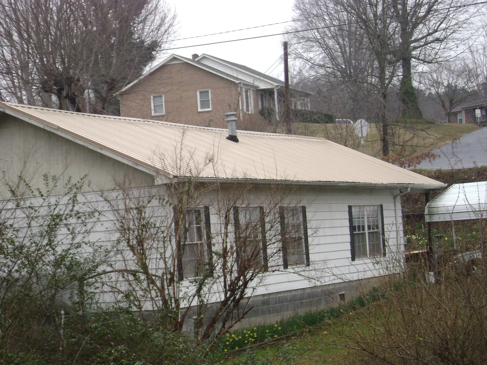 Tan metal roof on a white sided house set into a hillside — Commercial Roofing by Roofing Brothers in Saint Albans